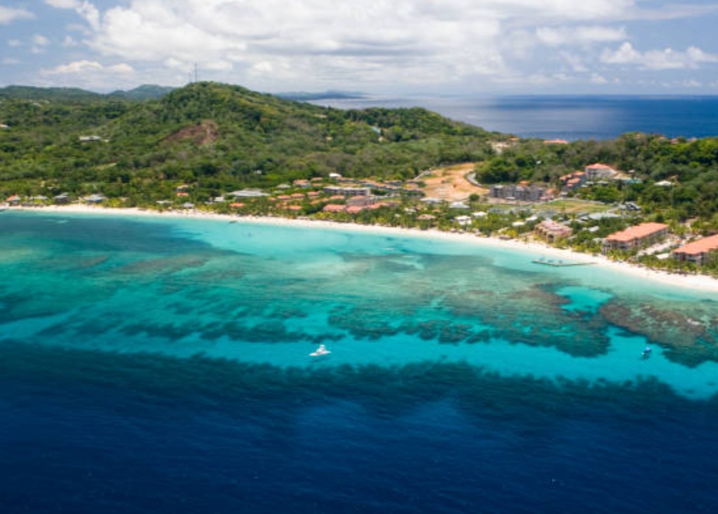 Aerial view of West Bay Beach Roatan Honduras with turquoise reef water, white sand and palm-lined resorts along the coastline